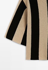 Écharpe large en tricot avec des rayures verticales alternées noires et beiges, montrant les détails texturés du fil.