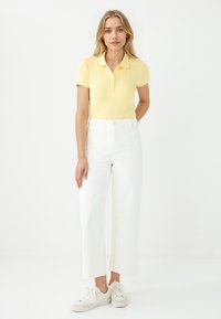 Polo shirt in morbido tessuto a righe giallo chiaro, abbinato a pantaloni bianchi a gamba larga e sneaker bianche. Design minimalista con colletto classico.
