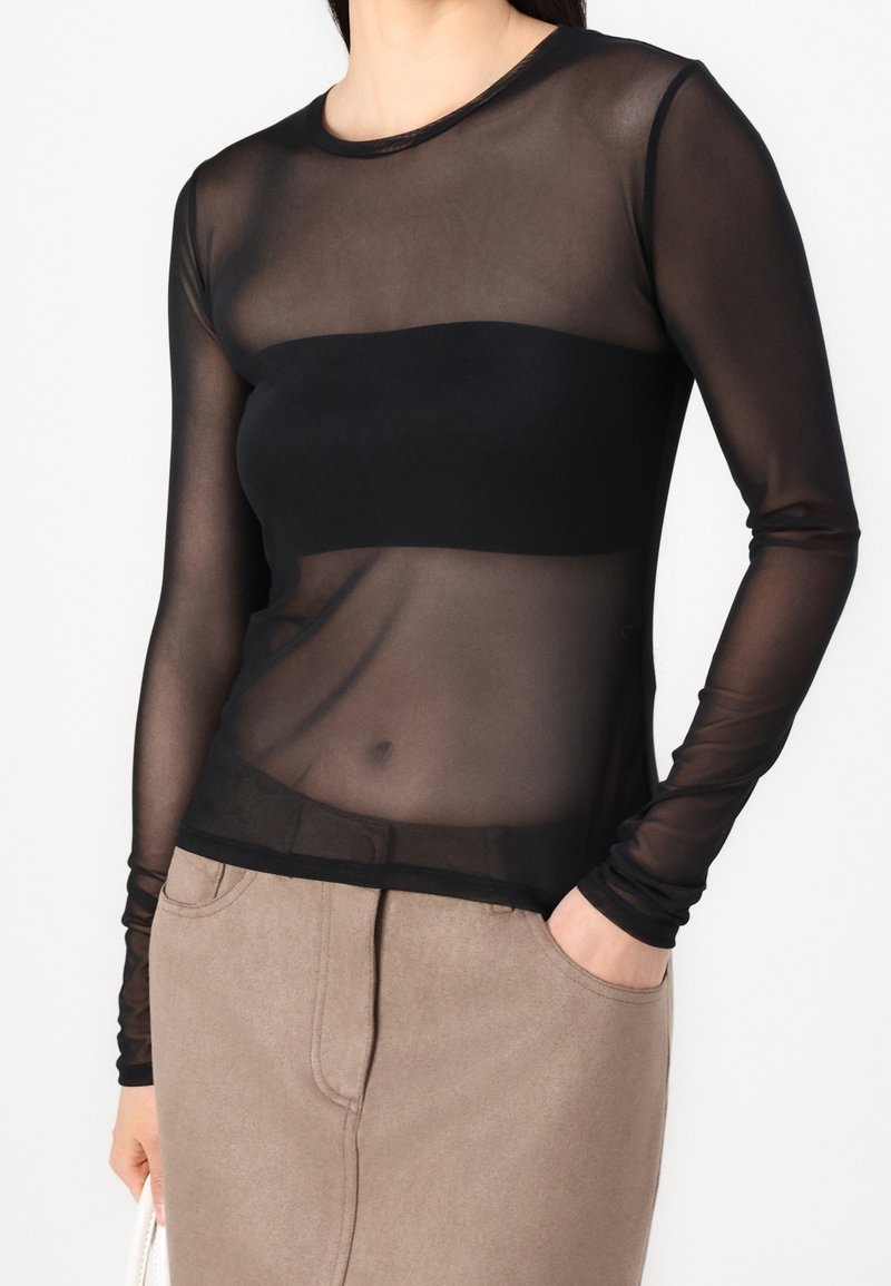Haut noir transparent à manches longues avec une bande noire ajustée à la taille, texture lisse et décolleté arrondi, associé à une jupe beige.