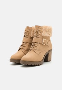 Tan ankle boots with faux fur collar, lace-up front, buckle accent, and textured heel. Made of suede-like material with a rugged sole.