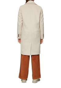 Beige Wollmischungsjacke mit taillierter Passform, Schlitz hinten und Dreiknopfdetail an den Ärmeln. Getragen über rostfarbenen Cordhosen.