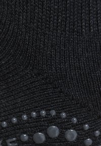 Tejido negro con textura que presenta un patrón acanalado, con acentos circulares de silicona brillantes fijados en el borde inferior.