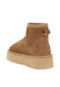 Stivaletto in suede marrone con suola beige spessa, con linguetta sul tallone e dettagli cuciti su sfondo bianco.