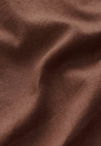 Brauner Leinenstoff mit leichtem Glanz, der eine weiche Textur und subtile Falten aufweist, die seine natürlichen Fasern und den leichten Fall zur Schau stellen.