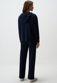 Felpa con cappuccio blu navy dal taglio rilassato, abbinata a pantaloni larghi texturizzati dello stesso colore; sneakers bianche completano il look.