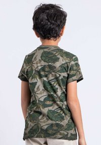 T-shirt à manches courtes dans une palette de couleurs vert et beige, présentant un motif de feuilles. Fabriqué en tissu doux avec un design col rond.