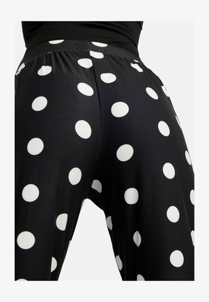 Zwarte broek met hoge taille en grote witte polkadots, gedragen met een zwart shirt, gezien van achteren van de taille tot halverwege het bovenbeen.