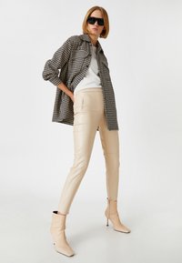 Sort og hvid houndstooth skjorte, hvid sweater, cremefarvede læderbukser, beige ankelstøvler med spids tå og overdimensionerede sorte solbriller.