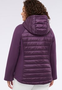 Chaqueta púrpura con capucha acolchada y textura acolchada en la parte posterior. Tejido frontal suave y mangas ajustadas con un ligero vuelo en el dobladillo.