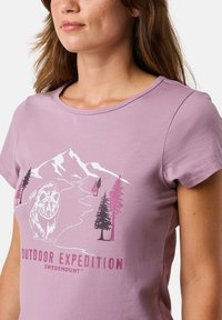 Lilla kortærmet t-shirt med et grafisk motiv af bjerge, en bjørn og træer i pink og hvid. Blødt, bomuldsagtigt stof.