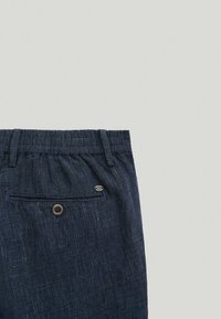 Granatowe spodnie z teksturowanym wzorem, wyposażone w elastyczną talię i tylnią kieszeń zabezpieczoną brązowym guzikiem.