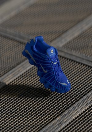 Blue athletic shoe with a mesh upper, textured design, and prominent sole featuring distinct cushioning elements and reflective accents.