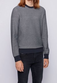 Pull en maille texturée bleu marine et gris clair avec poignets et ourlet côtelés, col rond et silhouette légèrement ajustée.