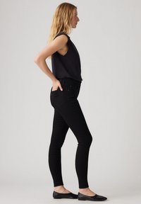 Jeans negros ajustados con una cintura alta, detalles en los bolsillos y textura suave. Combinados con una blusa sin mangas oscura y zapatos planos negros.