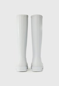 White rubber rain boots featuring a smooth texture, tall shaft, and a rounded toe. Vertical ridges run along the sides, highlighting the design.