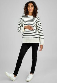 Gestreifter Pullover in Creme und Schwarz, lässige Passform, gerippte Bündchen und Saum. Kombiniert mit schwarzen engen Jeans und weißen Sneakers.