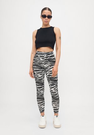 Svart, kort topp, joggebukser med zebra mønster i svart og hvitt, og hvite sneakers med tykk såle. Modellen har på seg svarte solbriller.