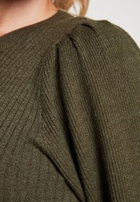 Primo piano di un tessuto a maglia verde oliva rigato con dettagli arricciati su una spalla.
