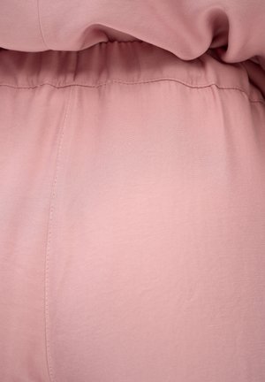 Miękka różowa tkanina z widocznymi szwami i detalem elastycznego paska w odzieży.