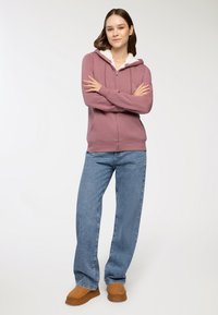 Felpa con cappuccio e zip in color malva, con interno in pile bianco, abbinata a jeans dritti azzurri e scarpe slip-on beige.