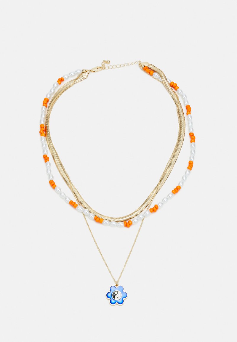 Colar em camadas em tom dourado, apresentando contas laranja, pérolas brancas e um pendente em forma de flor azul com um símbolo yin-yang.