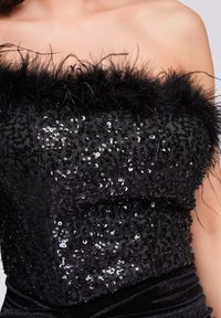 Top noir à sequins avec un bord en plumes au niveau du col, un corsage lisse et texturé, et une silhouette ajustée.
