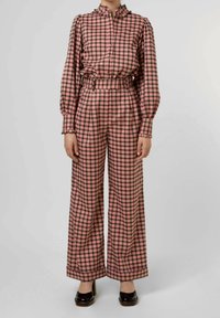 Outfit a quadretti composto da una camicia rosa e nera con colletto a volant e pantaloni larghi coordinati, realizzati in un tessuto lucido.
