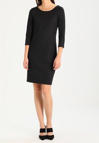 Czarna, dopasowana sukienka z rękawami o długości trzech ćwierć, okrągłym dekoltem i teksturowanym materiałem. Zestawiona z czarnymi, wysokimi szpilkami.