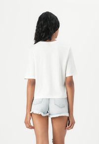 Witte katoenen t-shirt met korte mouwen en een ontspannen pasvorm, gecombineerd met lichtblauwe denim shorts met rafelige randen.
