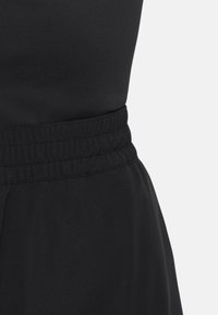 Gros plan sur une ceinture élastique noire d'un vêtement noir sur un fond gris clair uni.