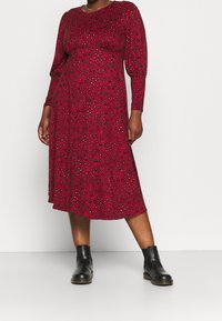 Robe rouge à manches longues avec un motif léopard, fabriquée en tissu doux, dotée d'un col rond et d'une coupe décontractée, associée à des bottines noires.