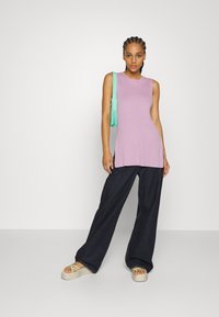 Top sem mangas de tom lilás claro com tecido canelado, combinado com jeans largos escuros e sandálias de plataforma bege com alças verdes; a segurar uma bolsa verde menta.