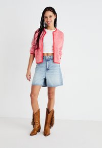 Roza rebrasta kardigan, bijeli crop top, plave traperice i smeđe frčke čizme. Naglasak na teksturama i kontrastnim bojama.