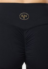 Leggings neri con un design arricciato sul retro, caratterizzati da un logo dorato in vita. Realizzati in un materiale liscio e elasticizzato.