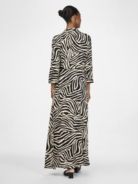 Vestido maxi em padrão zebra preto e creme, com mangas longas, um corte relaxado e uma silhueta fluida com uma abertura lateral.