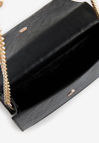 Juoda odinė rankinė su grandinėlės dirželiu, lygi tekstūra, apvalus auksinės spalvos metalinis dekoro elementas ir atvira vidinė dalis be matomų skyrių.