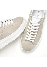Sneakers in suede beige chiaro con lacci bianchi e suola in gomma. Presentano una punta arrotondata e una marcatura minimale sul lato.