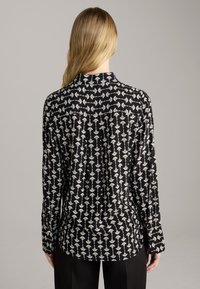 Black long-sleeve shirt featuring a white floral pattern, with a collared neck, smooth texture, and a slightly curved hem.