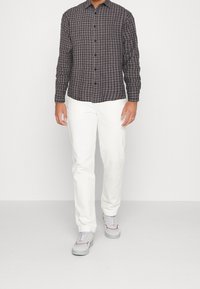 Schwarz-weiß kariertes Langarmhemd mit Kragen und Knopfleiste, kombiniert mit weißen, schmal geschnittenen Hosen und grauen Turnschuhen.