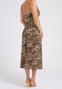 Robe midi à imprimé léopard avec bretelles fines, tissu lisse, corsage ajusté et jupe fluide. Associée à des talons beiges.