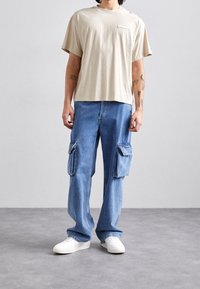 Beige bomuld t-shirt med korte ærmer og en brystlomme, parret med løs passende blå denim cargo bukser med lynlåslommer. Hvide sneakers.