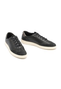 Baskets en cuir noir avec finition texturée, dotées d'un système de laçage, d'une semelle blanche et d'accents gris foncé contrastants.