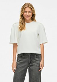 Pull blanc à manches courtes bouffantes. Tissu doux et lisse. Associé à un jean taille haute gris foncé. Design simple et moderne.