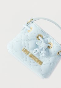 Τσάντα χειρός από γαλάζιο δερμάτινο με κεντητό σχέδιο, χρυσές μεταλλικές λεπτομέρειες και πλακέτα με λογότυπο. Διαθέτει μία λαβή στο πάνω μέρος.