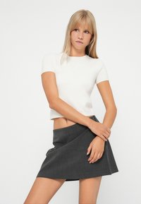 Hvit kort t-skjorte med korte ermer, kombinert med et svart og hvitt hundetannmønster mini skjørt med innpakningsdesign. Glatt stofftekstur.