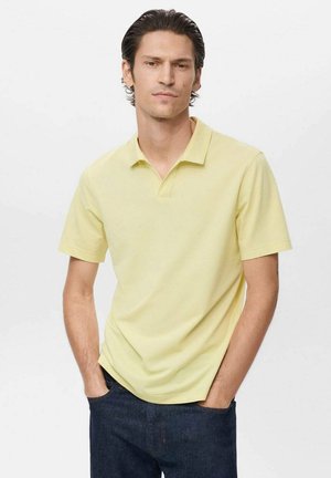 Polo de algodón suavemente amarillo con cuello clásico y mangas cortas, combinado con jeans oscuros, manos en los bolsillos. Diseño sencillo y limpio.