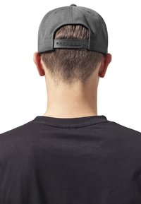 Casquette grise en tissu lisse avec une sangle en plastique ajustable à l'arrière, portée avec un t-shirt noir uni, montrant des cheveux coupés court.