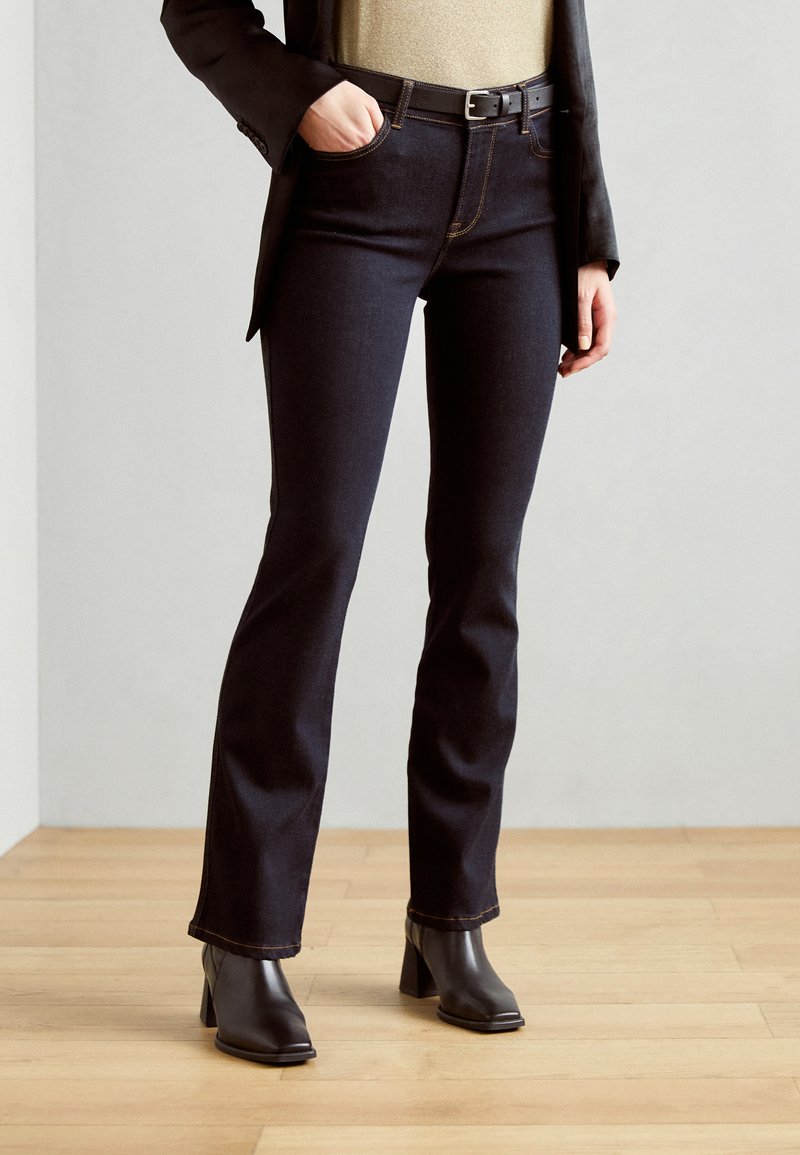 Mörka denimflaredjeans med kontrasterande sömmar, hög midja och framfickor, kombinerat med svarta klackade ankelstövlar.