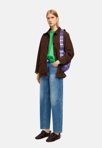 Brązowa zamszowa kurtka, zielony sweter z dzianiny, jasnoniebieskie szerokie dżinsy i ciemno-brązowe buty na sznurówki. Fioletowa torba ze srebrnym okuciem.