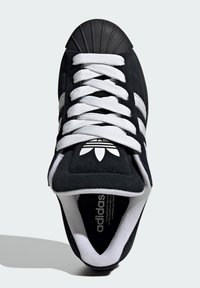 Čierna semišová teniska s bielymi šnúrkami a tromi pruhmi, vybavená gumovou špičkou na špičke a logom na jazyku, s textúrovaným vnútorným lemovaním.